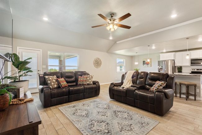Living room with light wood finished floors, ceiling fan, vaulted ceiling, and crown molding | Image 11