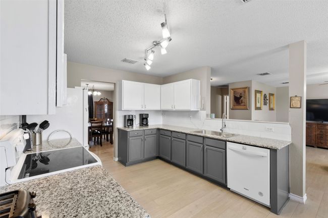 Kitchen with white appliances, gray cabinetry, light wood-type flooring, a textured ceiling, and white cabinets | Image 10