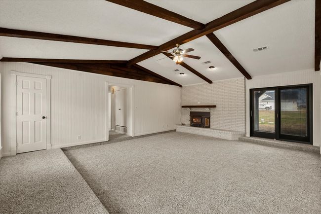 Unfurnished living room featuring ceiling fan, carpet flooring, a fireplace, and lofted ceiling with beams | Image 6