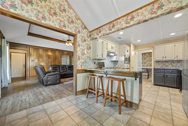 Kitchen with tasteful backsplash, a peninsula, under cabinet range hood, stainless steel microwave, and wallpapered walls | Image 12