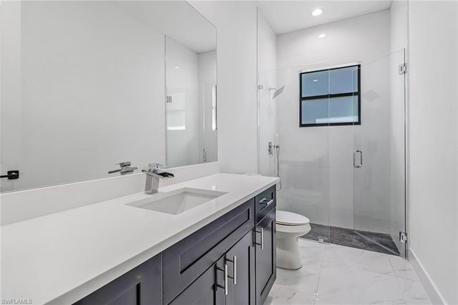 Bathroom with a shower with shower door, vanity, tile patterned floors, and toilet | Image 34