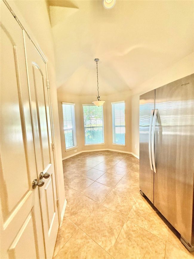 Bright breakfast nook with large windows and a hanging light fixture. It features tiled flooring and is adjacent to a modern stainless steel refrigerator. | Image 5