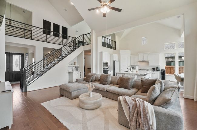 Living room featuring high vaulted ceiling, ceiling fan, stairs, dark wood-style flooring, and baseboards | Image 4