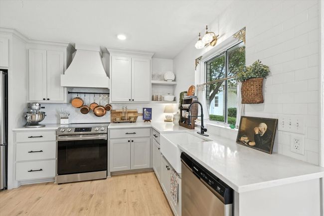 Kitchen with stainless steel appliances, light wood-style floors, custom exhaust hood, open shelves, and white cabinets | Image 13