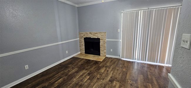 Unfurnished living room featuring wood finished floors, a textured wall, ornamental molding, and a stone fireplace | Image 5
