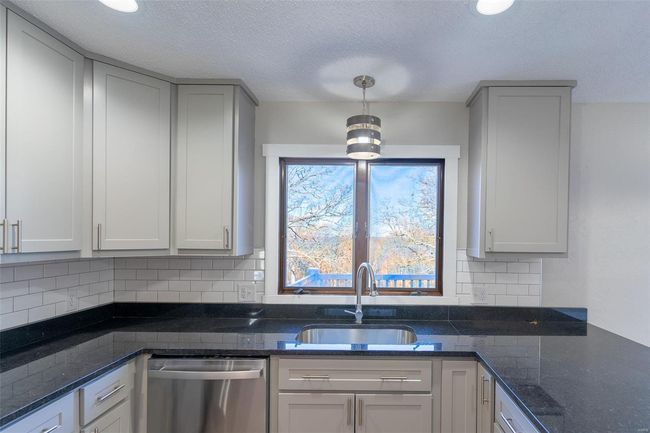 Kitchen with sink, stainless steel dishwasher, dark stone countertops, tasteful backsplash, and decorative light fixtures | Image 42
