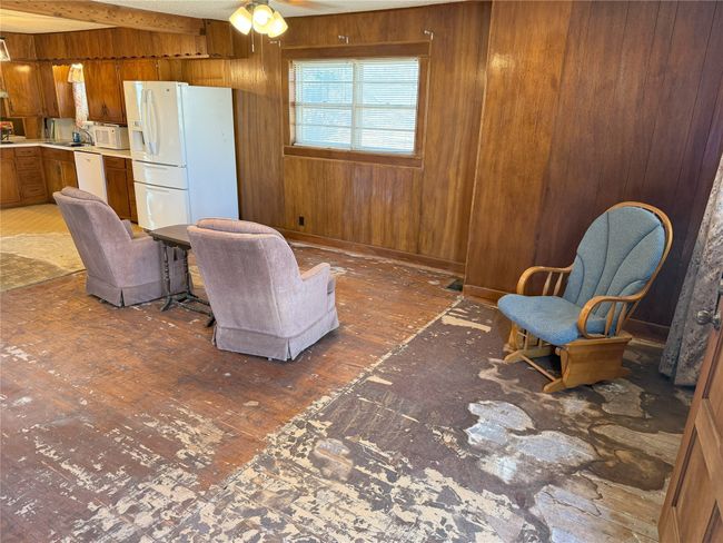 Living room featuring ceiling fan, wood paneled walls, beamed ceiling, and original wood floors ready for refinishing! Plenty of room for additional dining area. | Image 12