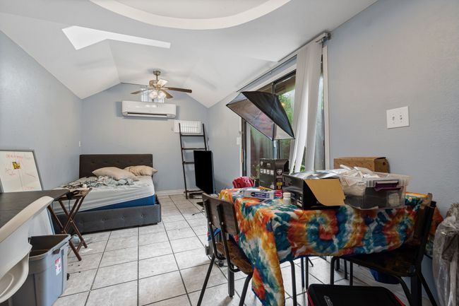 Bedroom with a wall mounted air conditioner, a skylight, vaulted ceiling, light tile patterned floors, and ceiling fan | Image 24