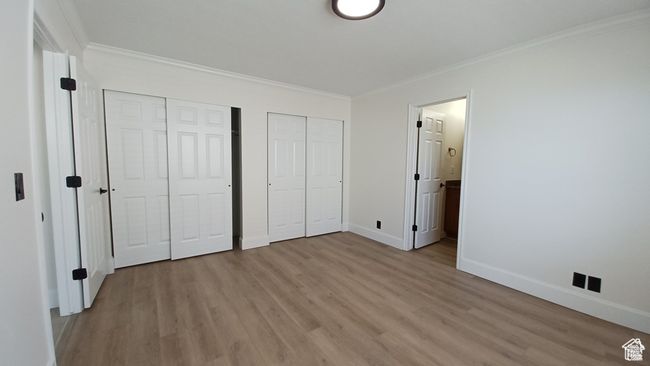 Unfurnished bedroom featuring multiple closets, light wood-type flooring, crown molding, and ensuite bath | Image 18