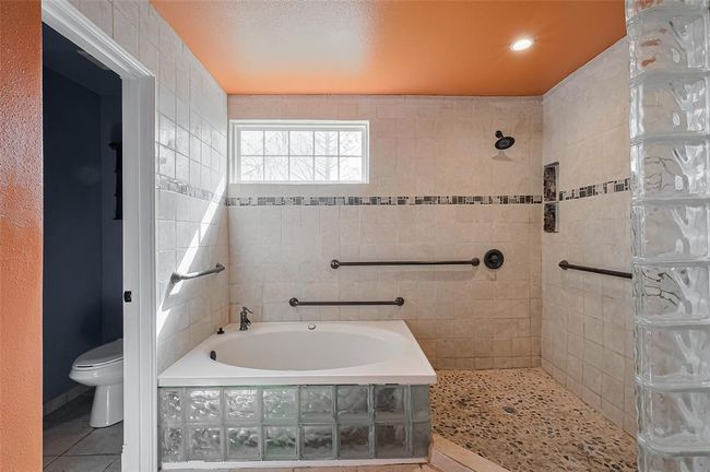Perfect for relaxation, this bath offers a spa-like atmosphere with a soaking tub surrounded by frosted glass block, paired with a spacious walk-in shower and modern tilework. | Image 35