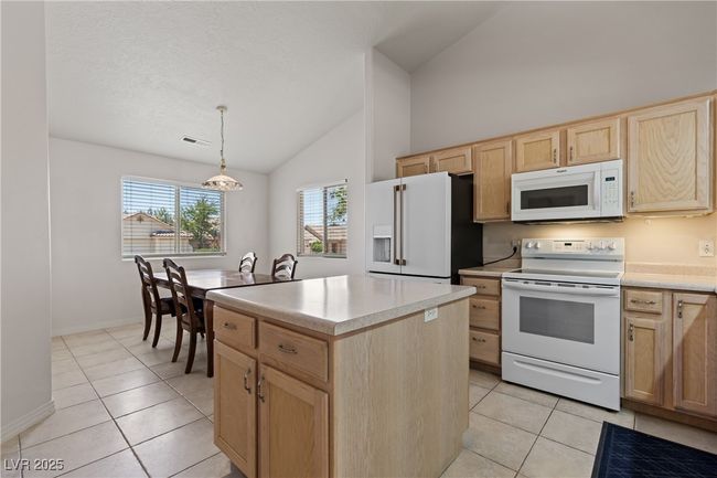 Kitchen featuring white appliances, light brown cabinetry, light tile patterned floors, a kitchen island, and high vaulted ceiling | Image 14