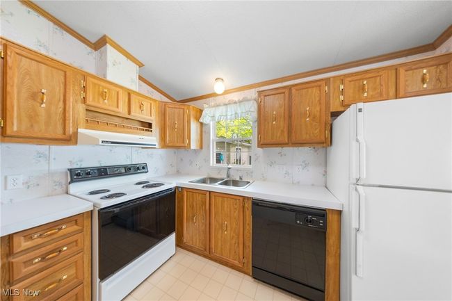 Kitchen featuring white appliances, wooden cabinets, sink, exhaust hood, lofted ceiling, and wallpapered walls | Image 8
