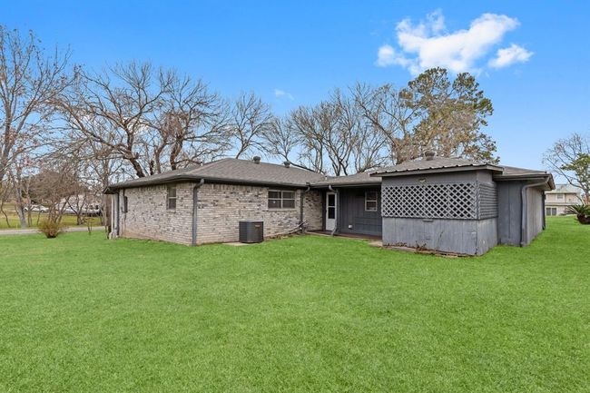 This photo shows a single-story brick home with a spacious backyard with a small covered patio area. The yard is well-maintained and surrounded by mature trees, offering a serene outdoor space. | Image 36