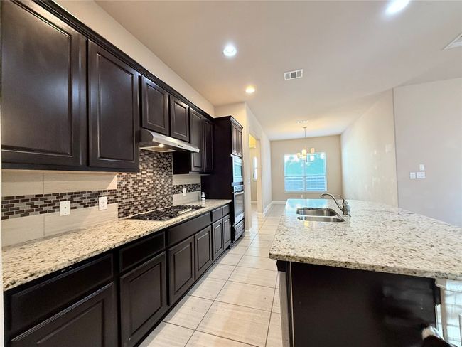 Kitchen featuring an island with sink, a chandelier, backsplash, recessed lighting, and light stone countertops | Image 16