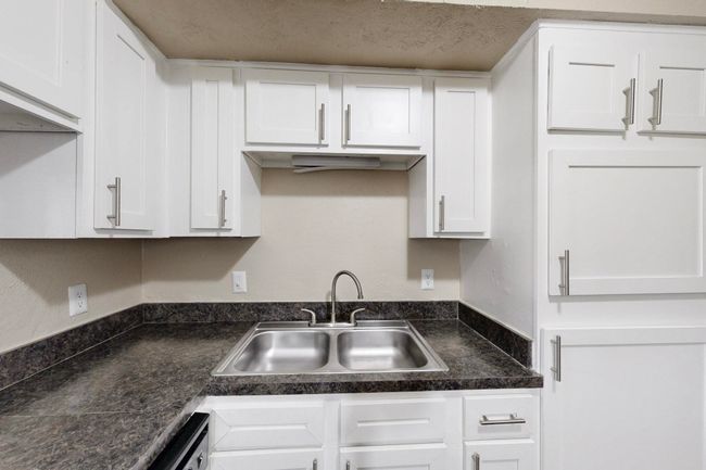 Kitchen featuring dark countertops, white cabinets, a textured ceiling, and a sink | Image 24