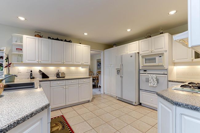 Kitchen featuring white appliances, white cabinetry, a sink, and decorative backsplash | Image 12