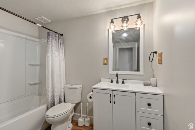 Full bathroom featuring visible vents, toilet, shower / tub combo with curtain, a textured ceiling, and vanity | Image 22