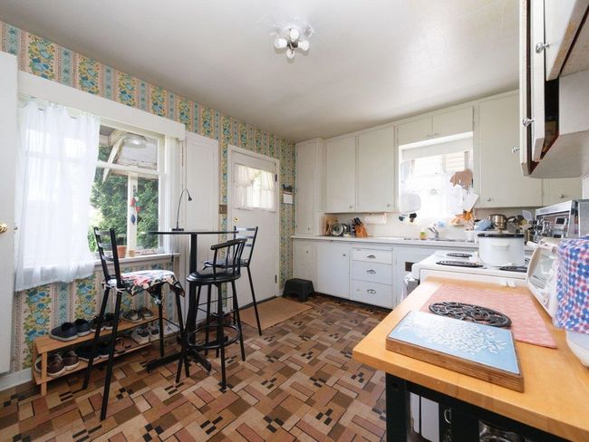 Kitchen with wallpapered walls, plenty of natural light, white cabinets, and light countertops | Image 10