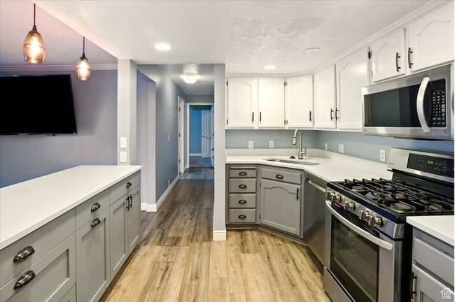 Kitchen featuring appliances with stainless steel finishes, a sink, gray cabinetry, light wood-style flooring, and light countertops | Image 8