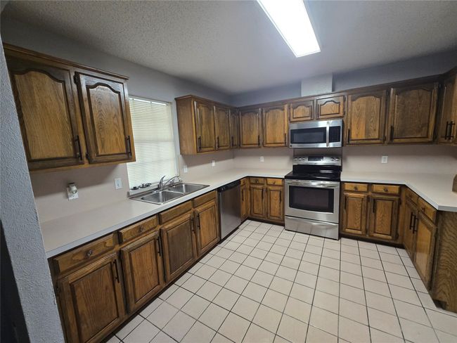 Kitchen with appliances with stainless steel finishes, light tile patterned flooring, light countertops, and a textured ceiling | Image 8