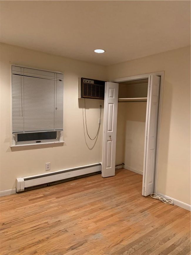 1st Fl Unfurnished bedroom with light wood-type flooring, an AC wall unit, baseboard heating, and a closet | Image 17