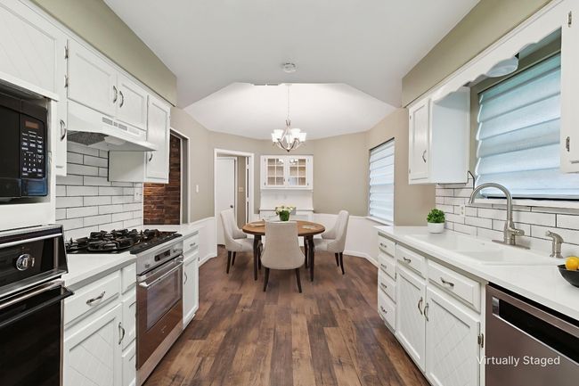 Kitchen featuring stainless steel appliances, under cabinet range hood, decorative backsplash, and white cabinets | Image 12