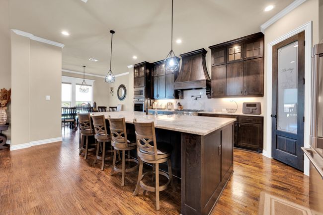Kitchen featuring ornamental molding, dark brown cabinets, decorative backsplash, custom exhaust hood, and a breakfast bar | Image 12