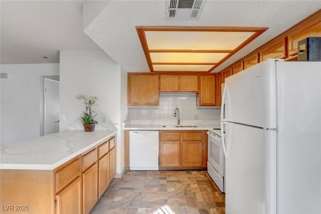 Kitchen featuring white appliances, a peninsula, light countertops, visible vents, and a sink | Image 14