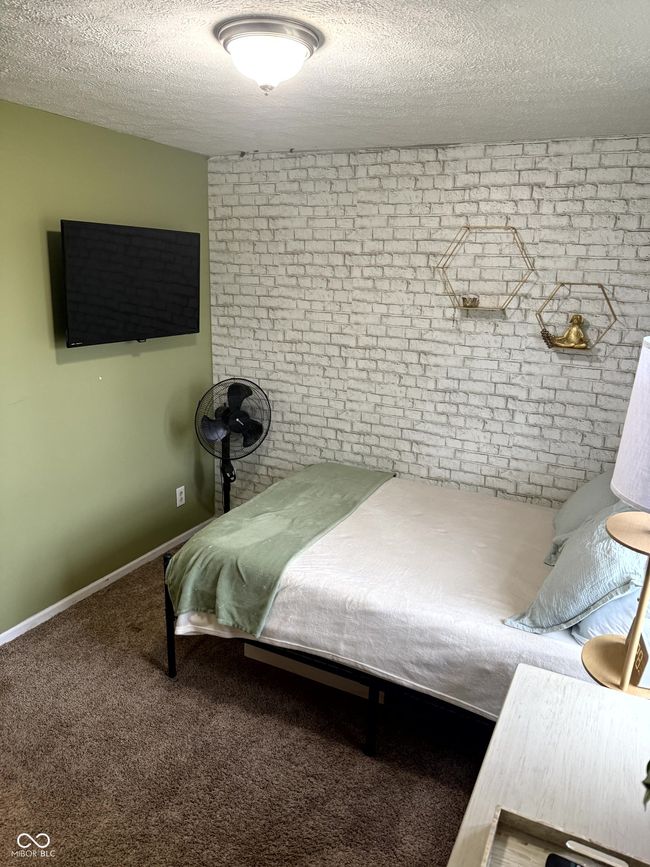 carpeted bedroom featuring a textured ceiling, brick wall, and baseboards | Image 16