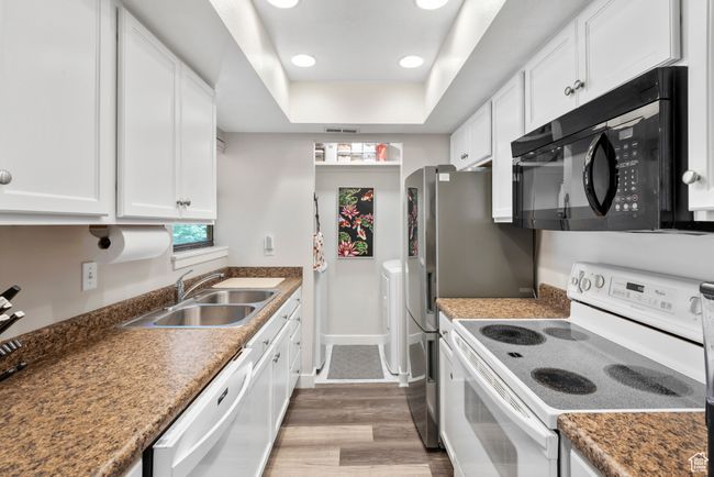 Kitchen featuring white appliances, white cabinets, wood finished floors, a raised ceiling, and recessed lighting | Image 16