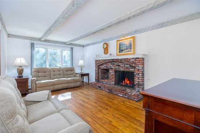 Living room with wood finished floors, beamed ceiling, a fireplace, and a baseboard radiator | Image 7