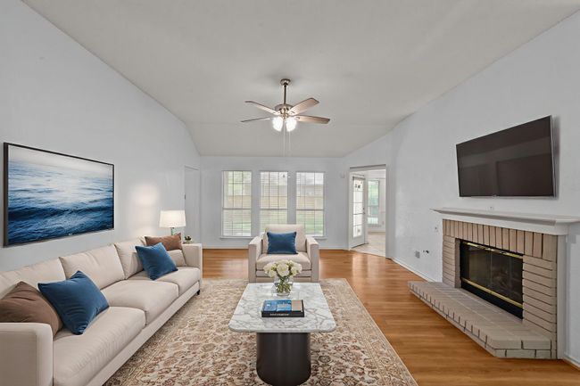 Living area with vaulted ceiling, wood finished floors, a brick fireplace with gas logs | Image 5