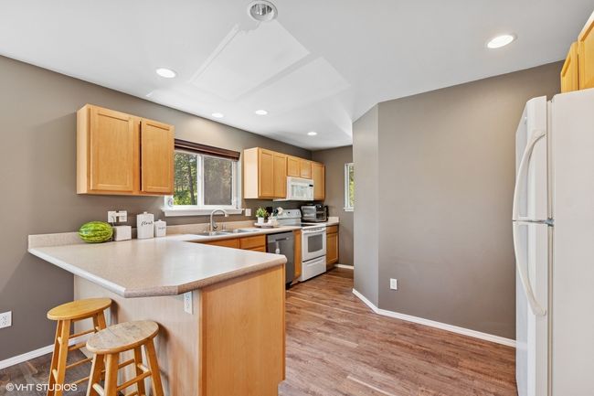 Kitchen with white appliances, a sink, light brown cabinetry, a breakfast bar area, and a peninsula | Image 7
