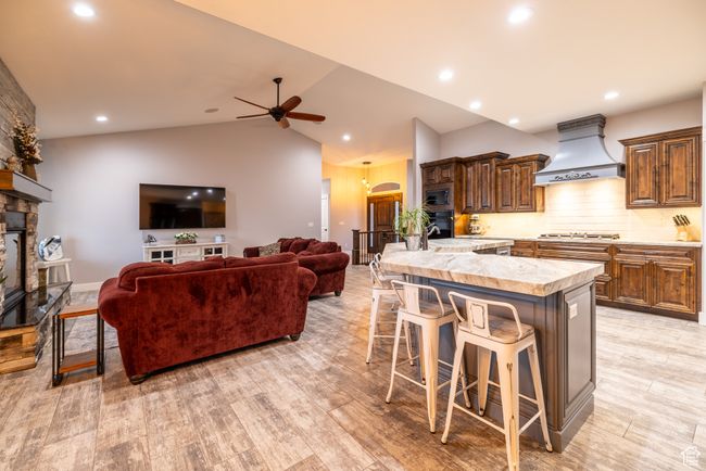 Kitchen featuring custom range hood, a kitchen bar, a stone fireplace, light countertops, and a ceiling fan | Image 18