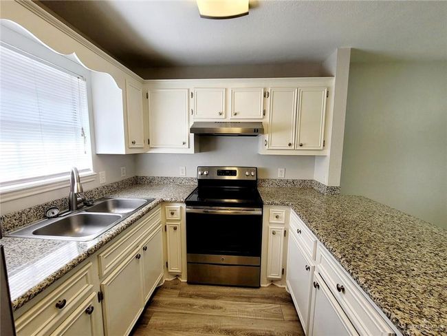 Kitchen with stainless steel range with electric stovetop, under cabinet range hood, wood finished floors, light stone countertops, and white cabinetry | Image 13