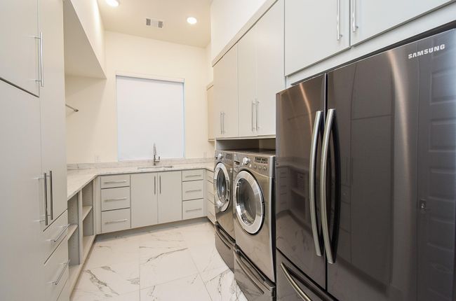 Oversized laundry room with sleek stainless steel appliances, ample cabinet storage, and a clean, bright design featuring a convenient countertop workspace. | Image 42