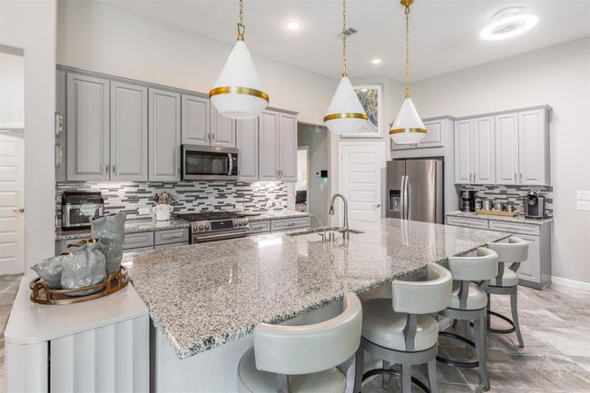 Visualize a spacious and modern kitchen where the focal point is a large, elegant kitchen island. Above the island, upgraded pendant lights cast a warm and inviting glow, highlighting its impressive size and design. | Image 15