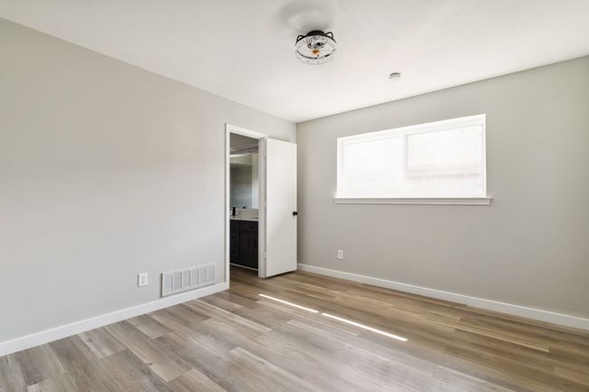 Unfurnished bedroom with wood finished floors, visible vents, ensuite bath, and baseboards | Image 23