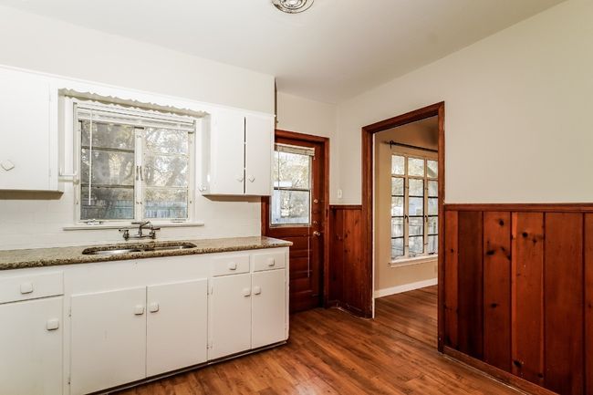 Kitchen with a wainscoted wall, wood finished floors, white cabinets, decorative backsplash, and wooden walls | Image 14