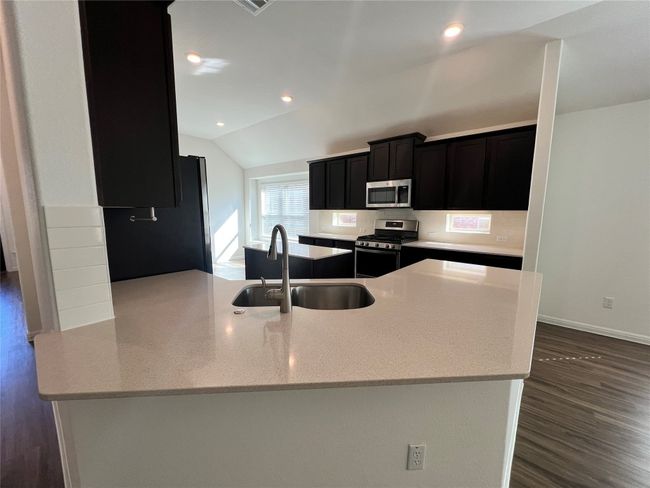 Kitchen featuring dark cabinets, lofted ceiling, dark wood-type flooring, light stone countertops, and appliances with stainless steel finishes | Image 16