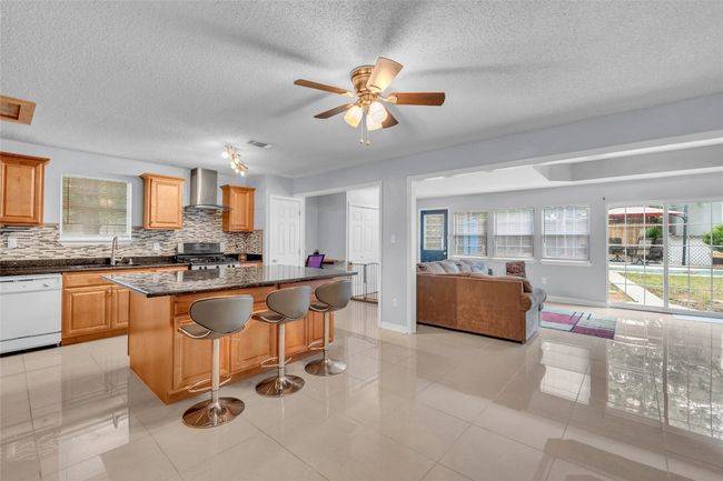 Kitchen featuring white dishwasher, backsplash, wall chimney exhaust hood, and open floor plan | Image 21