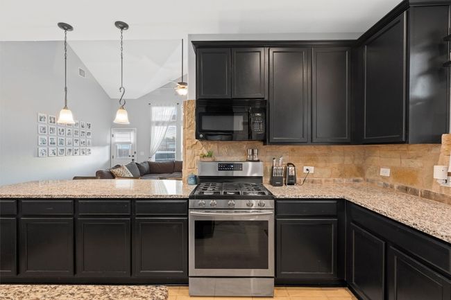 Kitchen featuring stainless steel gas range, black microwave, dark cabinetry, decorative backsplash, and lofted ceiling | Image 7