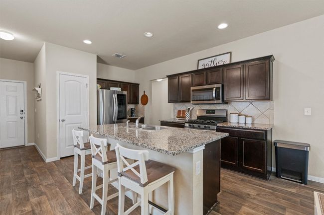 Kitchen with stainless steel appliances, dark brown cabinets, tasteful backsplash, an island with sink, and dark wood finished floors | Image 6