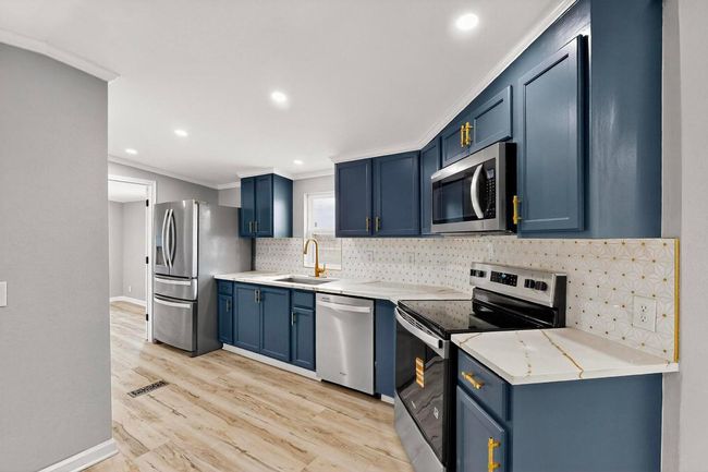 Kitchen with stainless steel appliances, a sink, blue cabinetry, ornamental molding, and tasteful backsplash | Image 19