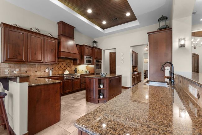 Kitchen with a raised ceiling, a sink, a center island, granite countertops, and backsplash | Image 10