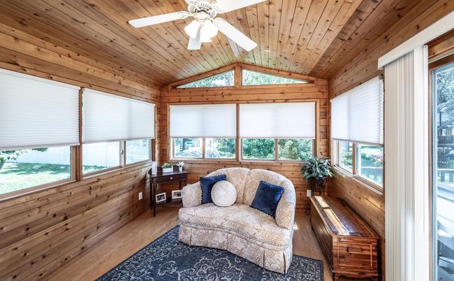Gorgeous cedar vaulted four-season porch with windows on three sides & sliding door to deck features engineered hardwood flooring, attractive triangular windows above windows on back wall, ceiling fan with lights and new custom blinds & verticals. | Image 13