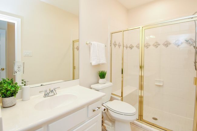 This bathroom features a clean, modern design with a large mirror, white vanity, and glass-enclosed shower. The neutral color palette and decorative tiles add a touch of elegance. | Image 24