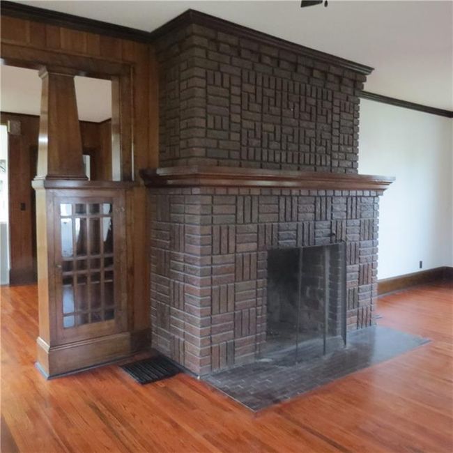Room details with built in glass display cabinets, wood finished floors, crown molding, and a brick fireplace | Image 6