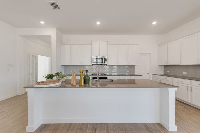 Kitchen featuring stainless steel microwave, tasteful backsplash, white cabinetry, a center island with sink, and recessed lighting | Image 8