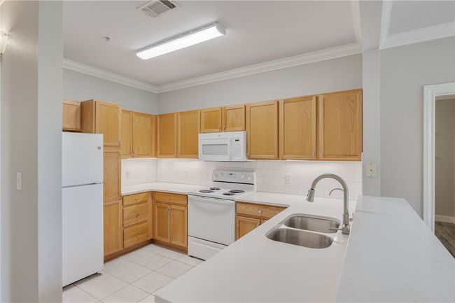Kitchen with white appliances, ornamental molding, tasteful backsplash, light countertops, and light tile patterned flooring | Image 5